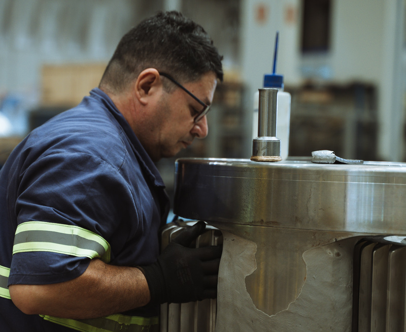 Técnico realizando manutenção em equipamento industrial de grande porte, destacando inspeção e ajuste de componentes críticos para evitar paradas não programadas.